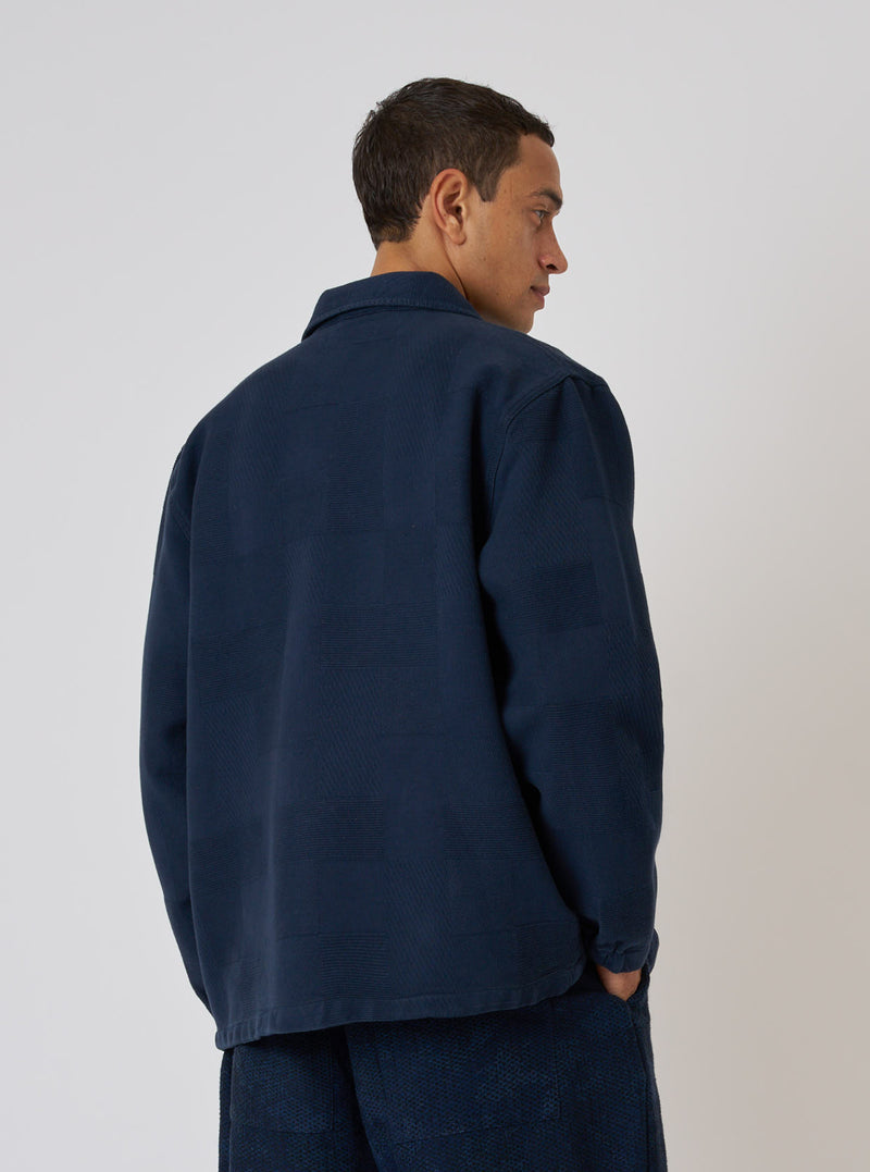 A man models the Dark Navy Patchwork Weave Cotton Labour Jacket against a plain backdrop. The jacket is a dark navy with a subtle patchwork weave.