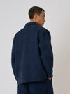 A man models the Dark Navy Patchwork Weave Cotton Labour Jacket against a plain backdrop. The jacket is a dark navy with a subtle patchwork weave.