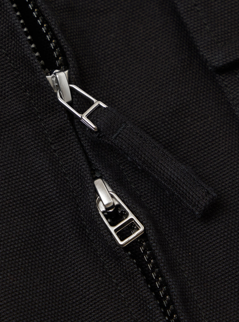 Close-up of the zipper on the Black Organic Canvas S130 Jacket. The black canvas material is visible, along with the silver zipper pull.