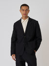 A model poses in a Black Organic Canvas Two Button Jacket against a white backdrop. The jacket is paired with a light-colored shirt for contrast.