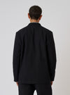Back view of a model wearing a Black Organic Canvas Two Button Jacket. The jacket is on a white background.