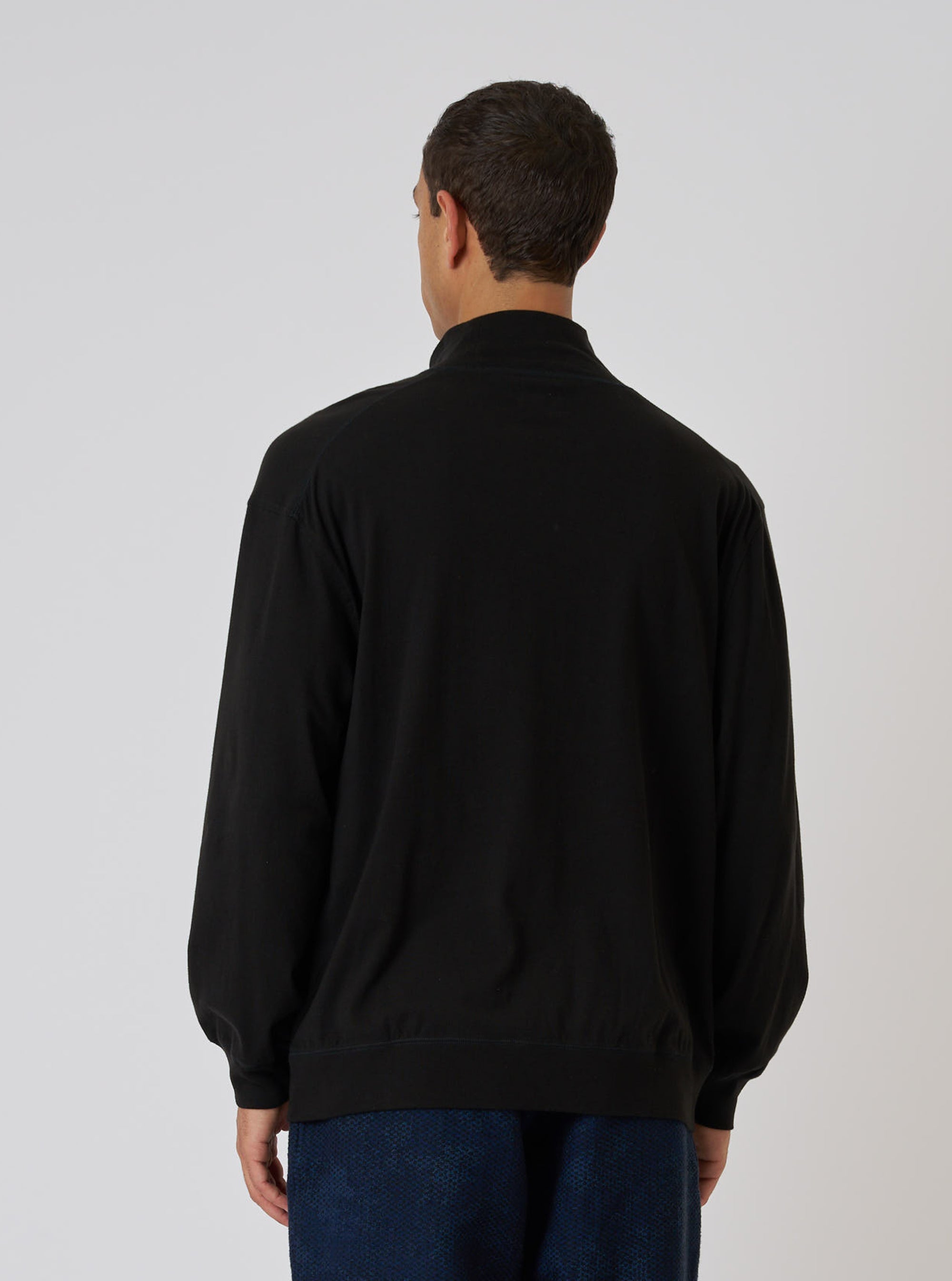 Back view of a model wearing a Black Single Jersey Funnel Neck Tee. The tee is black and made of soft jersey. The background is a clean, bright white.