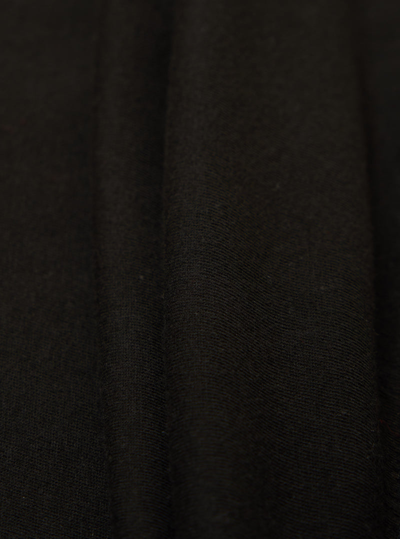 Close-up of the Black Single Jersey Funnel Neck Tee fabric. The soft, black jersey material is draped to show texture. Simple studio background.