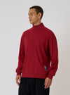 A man poses in a Red Single Jersey Funnel Neck Tee against a white backdrop. The tee has long sleeves and a relaxed fit. He wears dark pants. The image is well-lit.