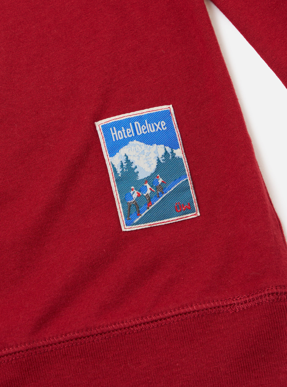 Close up of the red Single Jersey Funnel Neck Tee on a white background, showing the fabric texture and a Hotel Deluxe patch.