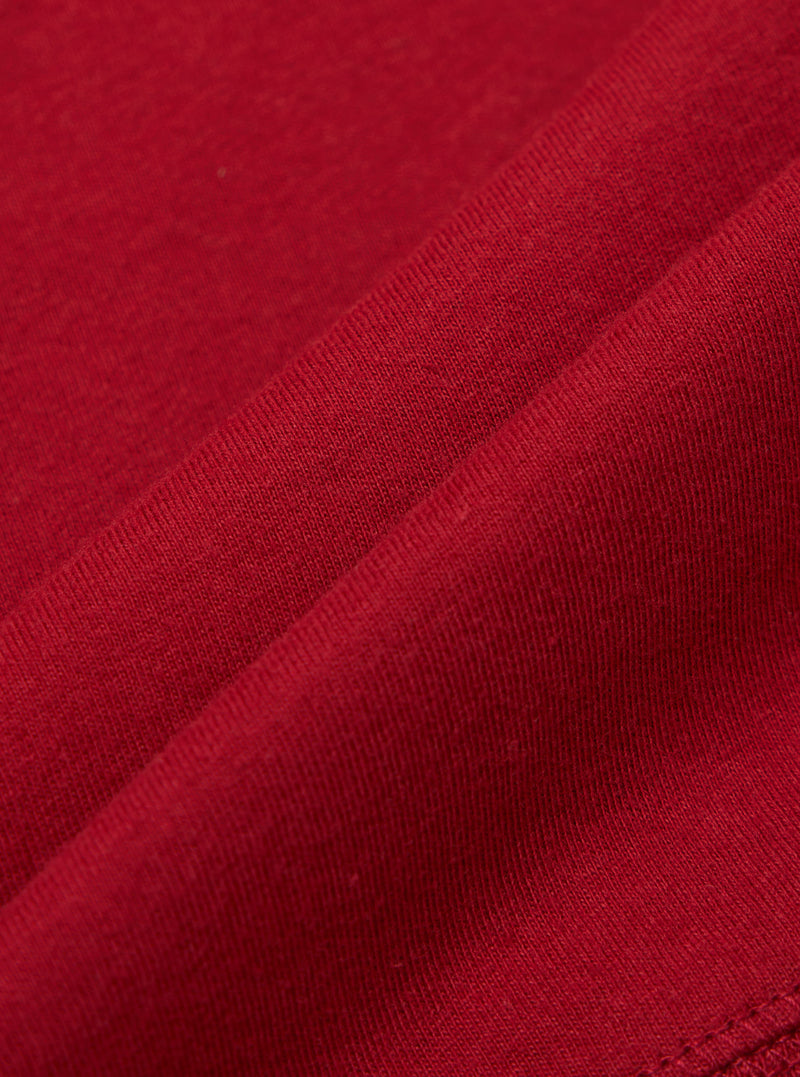 Close-up of the Red Single Jersey Funnel Neck Tee fabric. The soft, red jersey material is draped to show its texture and quality. The image highlights the tee's comfortable fit.