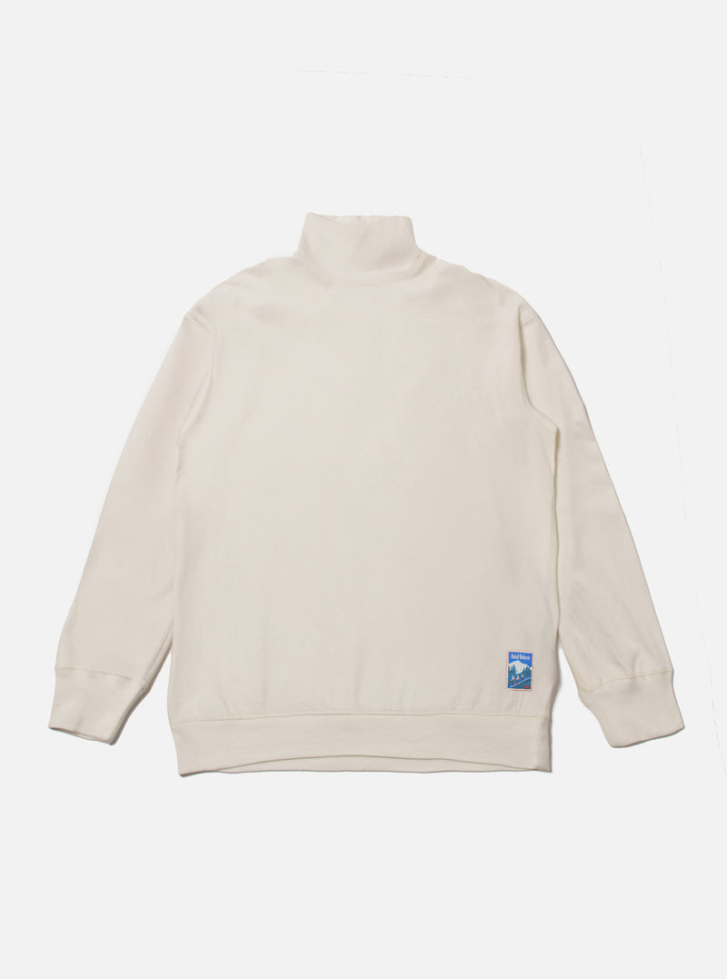 The Ecru Single Jersey Funnel Neck Tee, laid flat on a white background. The tee is a light cream color and has a funnel neck. A small blue logo is on the lower left.