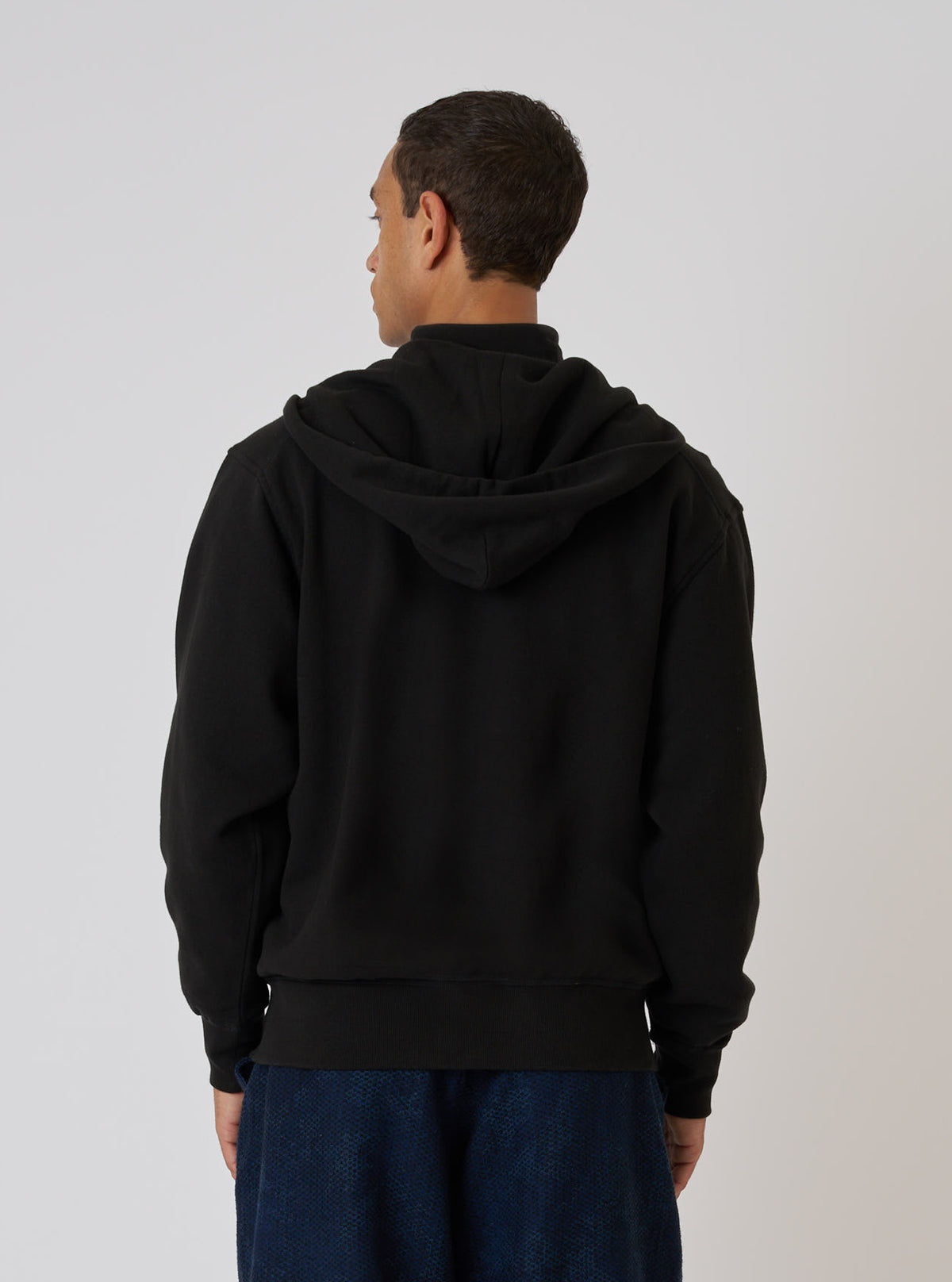 Back view of a model wearing a Black Brush Back Sweat New York Hoody. The black cotton hoody is set against a plain white background.