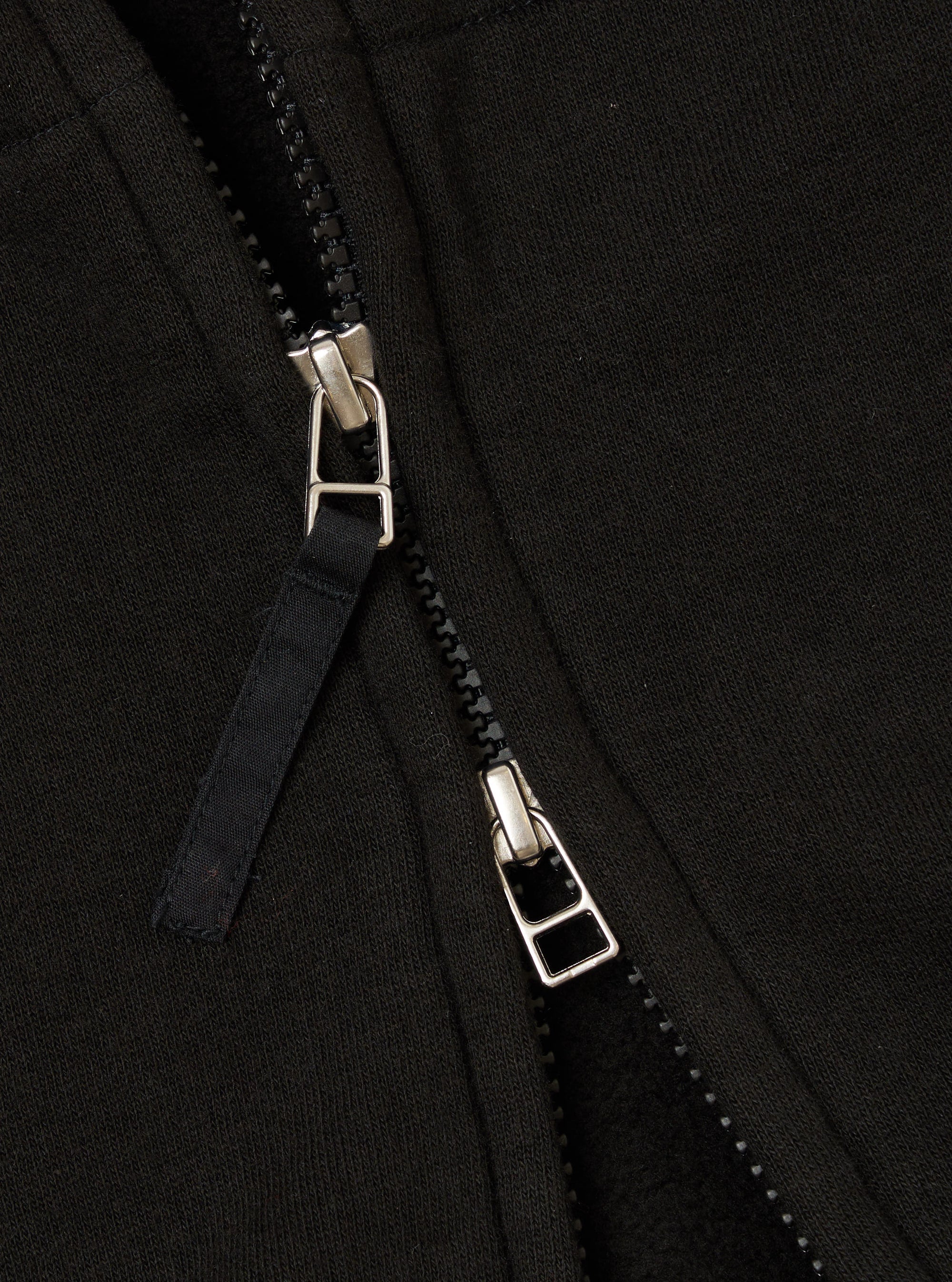 Close-up of the zipper on a Black Brush Back Sweat New York Hoody. The black fabric and silver zipper are detailed in this shot.