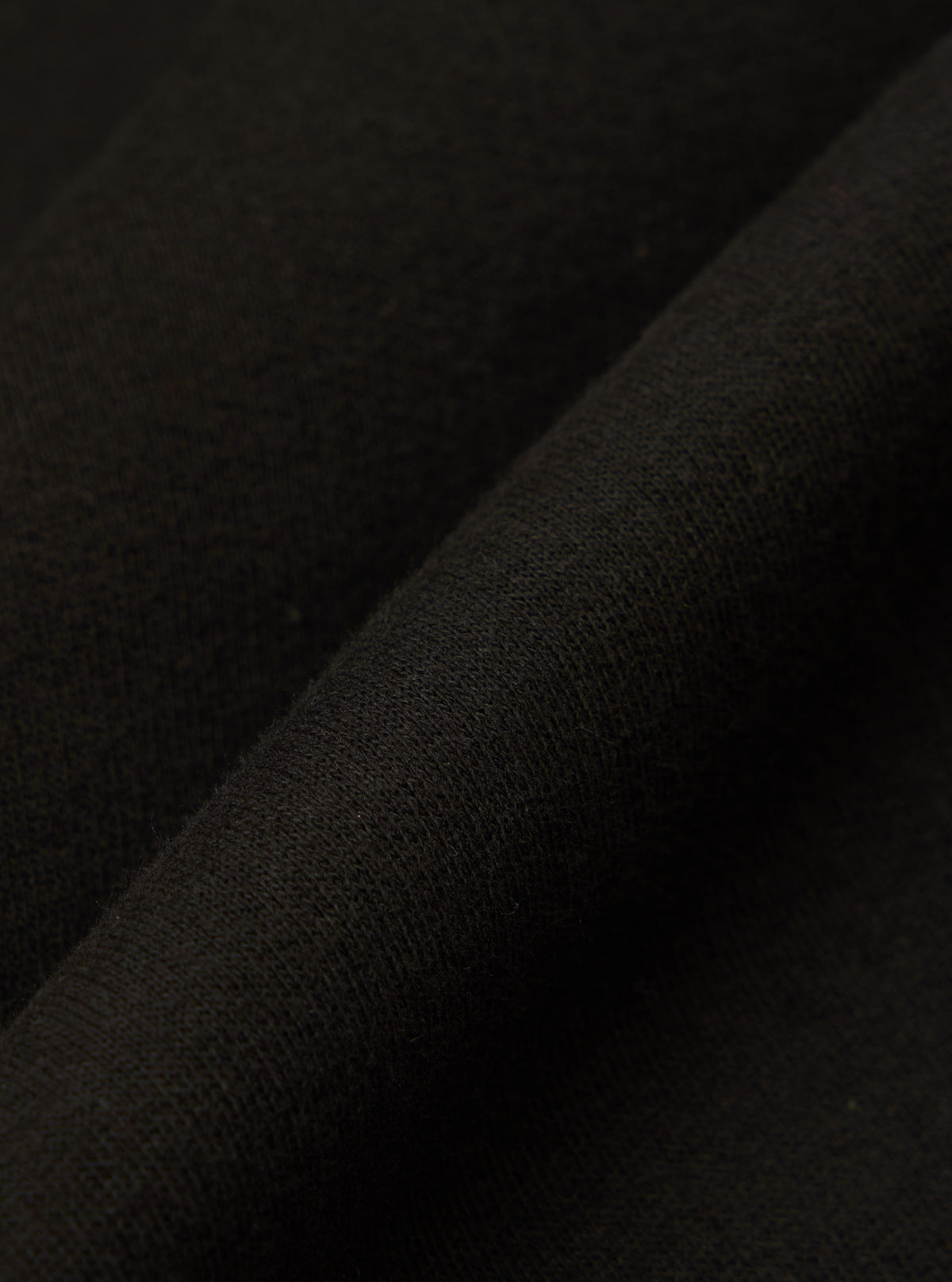 Close-up of the Black Brush Back Sweat New York Hoody fabric. The soft, black material is folded, showcasing its texture and quality.