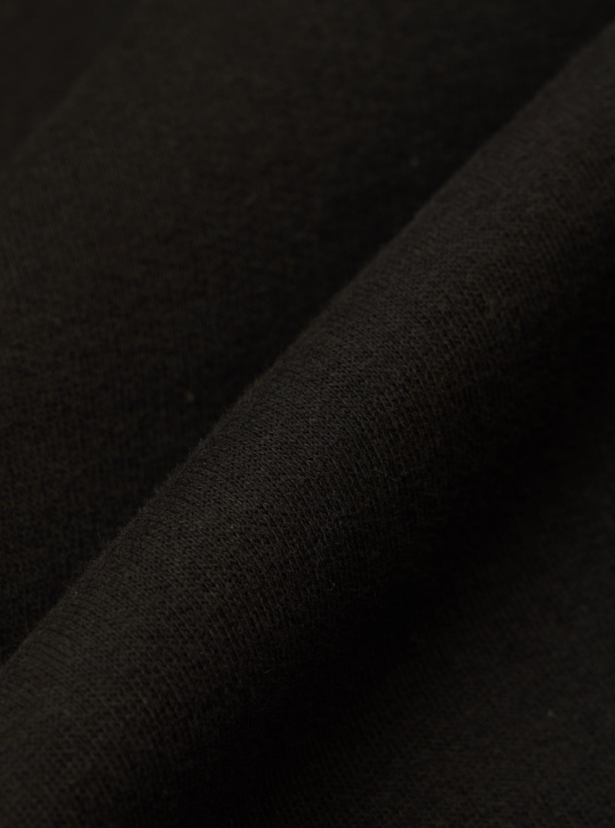 Close-up of the Black Brush Back Sweat New York Hoody fabric. The soft, black material is folded, showcasing its texture and quality.
