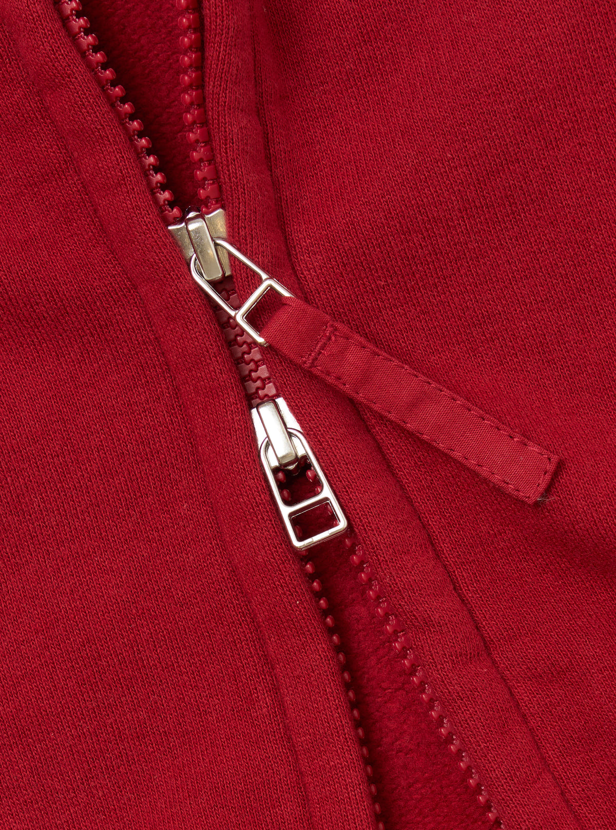 Close-up of the zipper on the Red Brush Back Sweat New York Hoody. The red fabric shows the texture of the material. The zipper is silver and red.