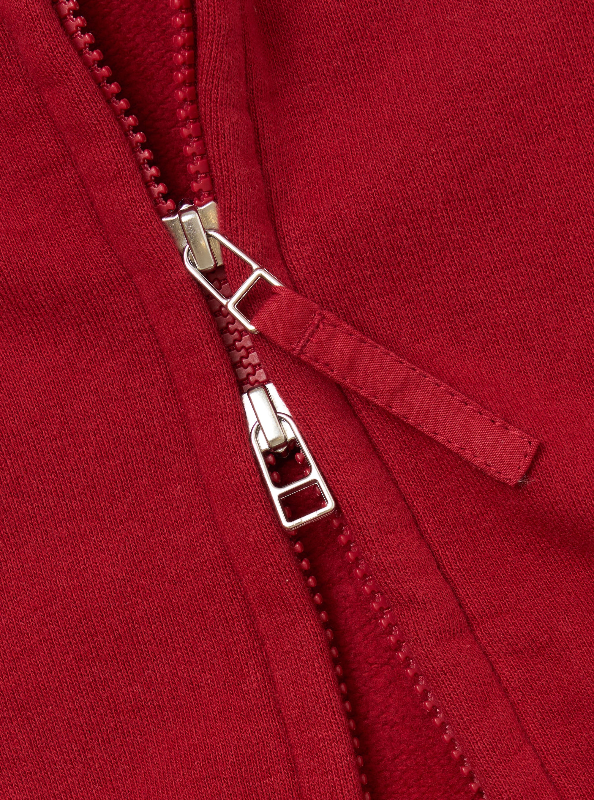 Close-up of the zipper on the Red Brush Back Sweat New York Hoody. The red fabric shows the texture of the material. The zipper is silver and red.