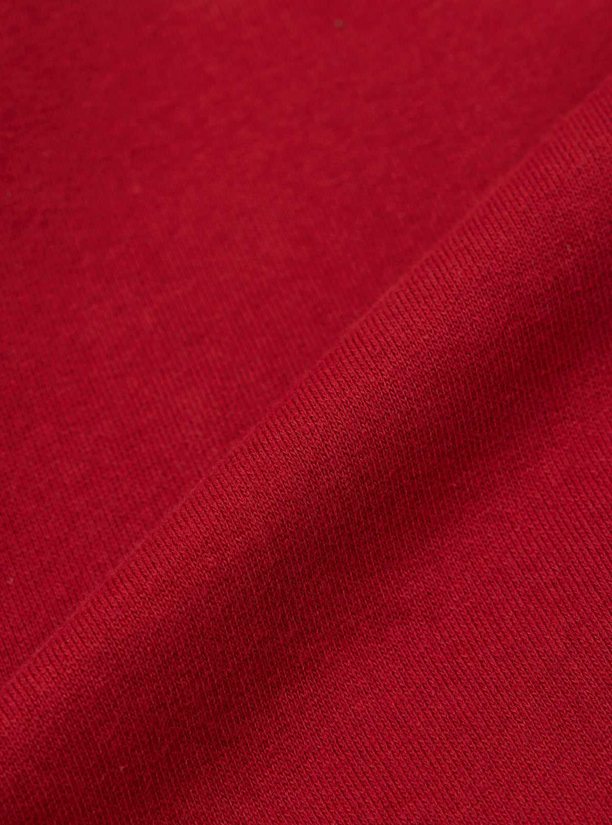Close-up of the red, textured fabric of the Red Brush Back Sweat New York Hoody. The material is folded, showing the weave. Background is a plain surface.