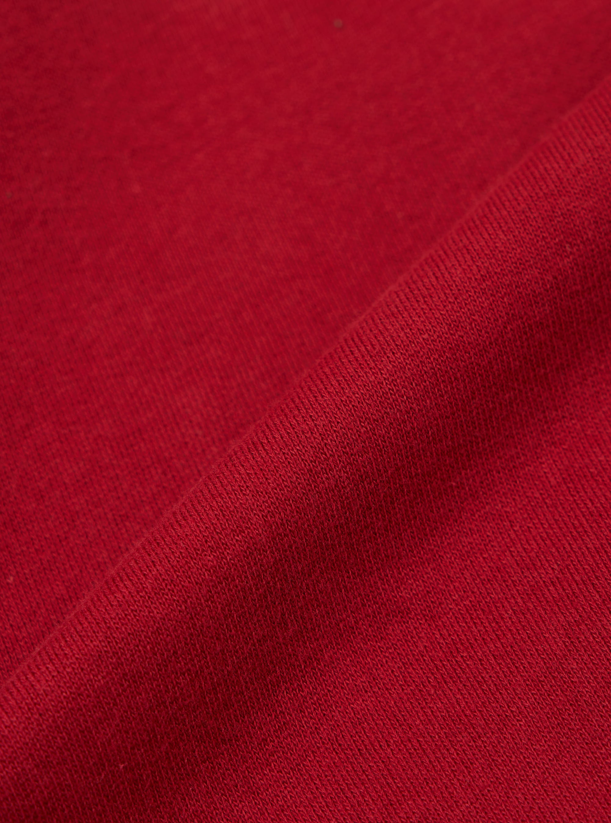 Close-up of the red, textured fabric of the Red Brush Back Sweat New York Hoody. The material is folded, showing the weave. Background is a plain surface.