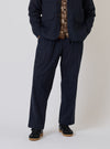 A model on a white background wears the Indigo Brushed Denim Oxford Pant. The pants are a relaxed fit and paired with a jacket and sneakers.