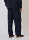 Back view of a model wearing the Indigo Brushed Denim Oxford Pant, styled with black shoes, against a plain backdrop. The pants have a relaxed fit.