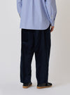 Back view of a model wearing the Navy Velveteen Oxford Pant. The pants are a loose fit and paired with a blue striped shirt and black shoes. Simple white background.