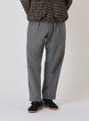 A model wears Charcoal Organic Chambray Oxford Pant in a studio setting. The pants are paired with black sneakers and a patterned jacket. The background is a clean, bright white.