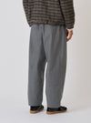 Back view of a model wearing the Charcoal Organic Chambray Oxford Pant. The pants are a loose fit and styled with a jacket. Shot against a plain background.