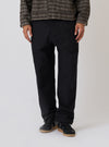 A model stands against a white backdrop wearing the Black Organic Canvas Super Chino. The chinos are paired with black sneakers and a patterned jacket.