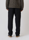 Back view of a model wearing the Black Organic Canvas Super Chino pants in a studio setting. The black chinos are paired with a patterned jacket and black sneakers.