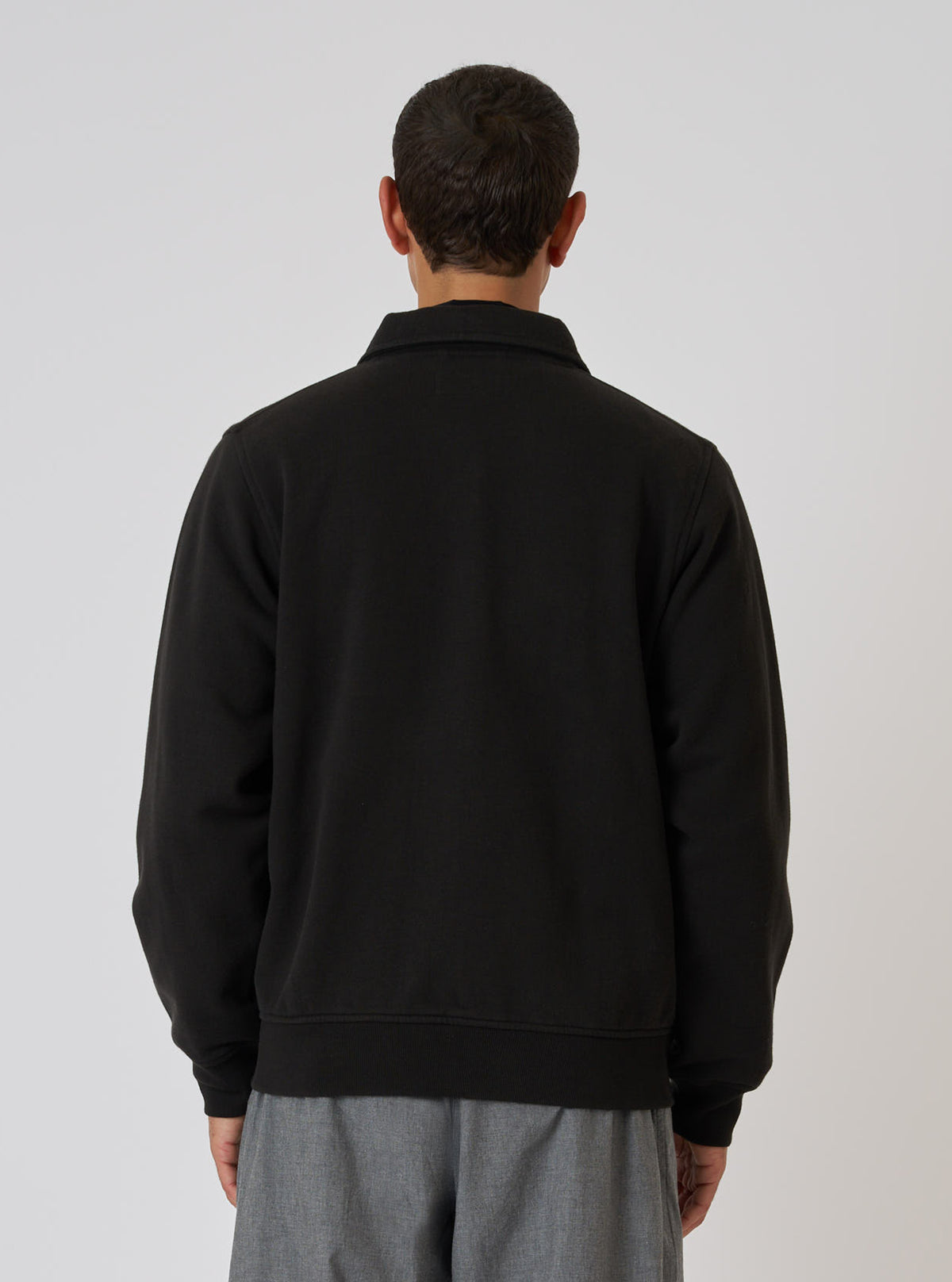 Back view of a model wearing the Black Brush Back Sweat Tyler Sweat Jacket. The jacket is black and the background is white.