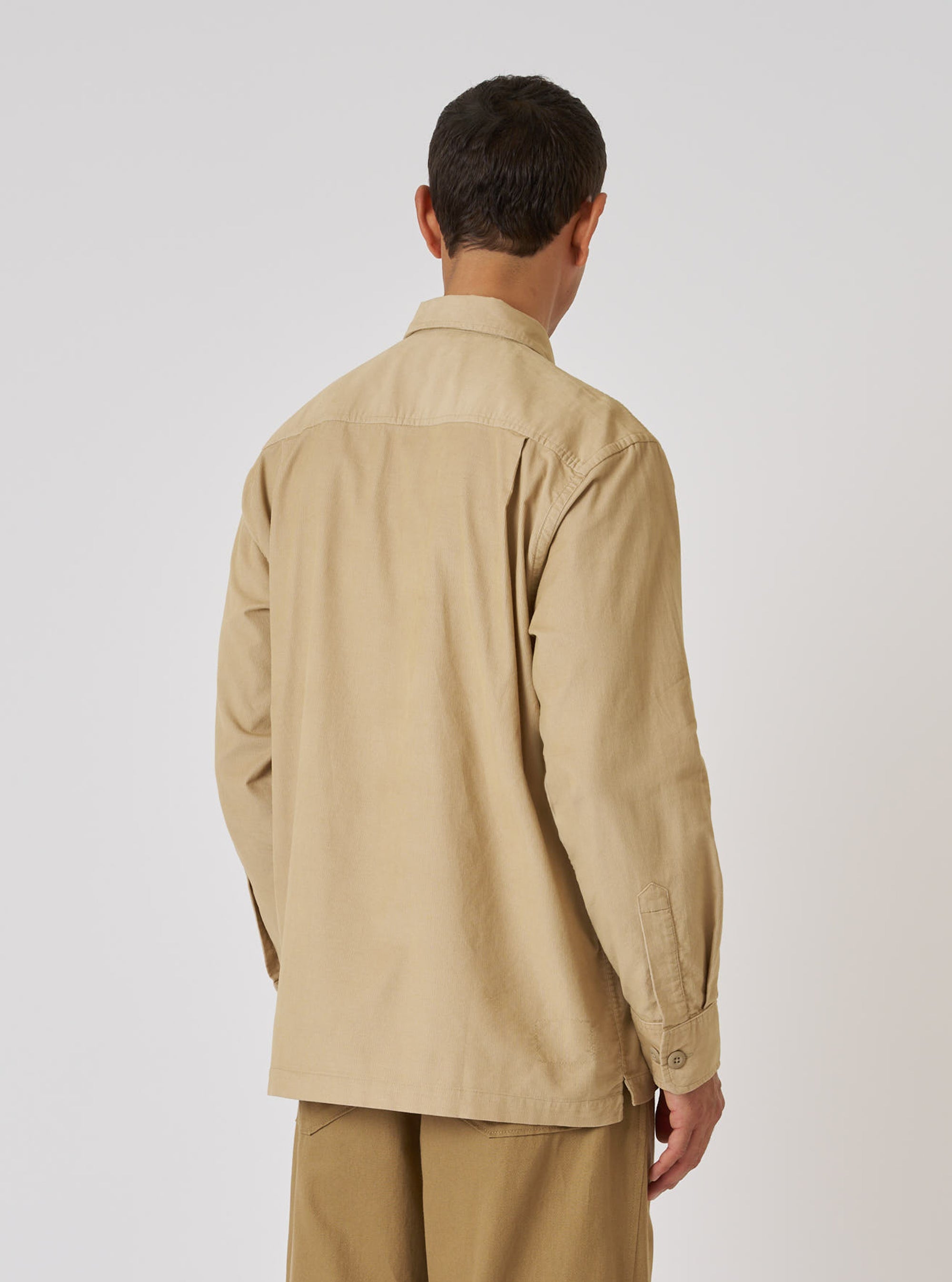 Back view of a man wearing the Sand Organic Fine Cord Fatigue Shirt. The shirt is a light tan color and made of corduroy. The background is a plain white.