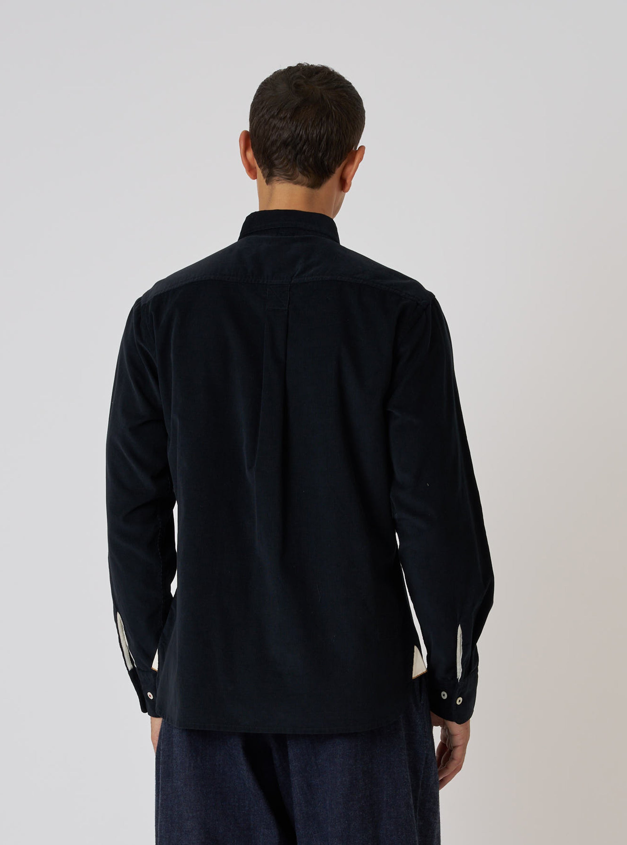 Back view of a model wearing a Black Organic Fine Cord Daybrook Shirt. The shirt is dark and made of corduroy. The background is a plain white.
