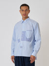 A model poses in front of a white background wearing a Blue Office Stripe Patched Lazy Day Shirt. The shirt is blue and white striped with light blue patches.