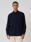 A model poses in front of a white background, wearing the Dark Navy Sid Flannel CPO Shirt. The shirt is a dark navy color and has two chest pockets with button closures.