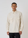 A man poses in the Ecru Sid Flannel CPO Shirt against a white backdrop. The shirt is a light, natural color with a relaxed fit. He's wearing dark pants.