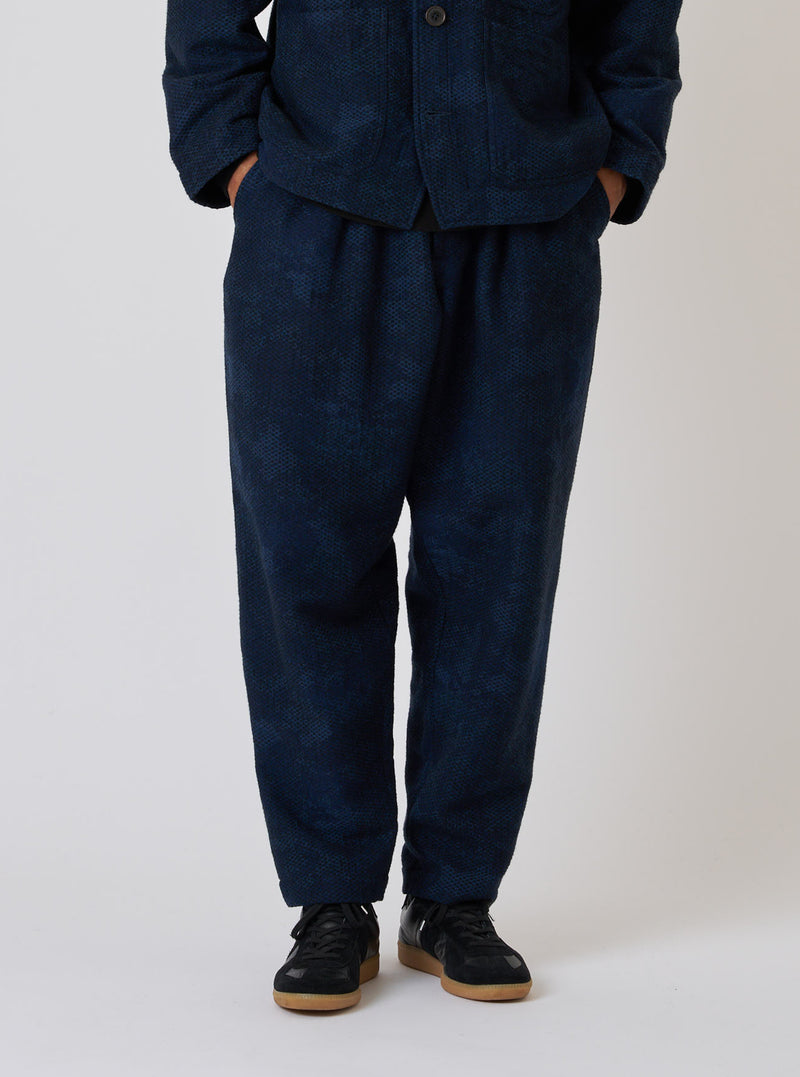 Studio shot of a model wearing Black/Indigo Denim Camo Pleated Track Pant. The indigo pants have a relaxed fit. Set against a plain white backdrop.