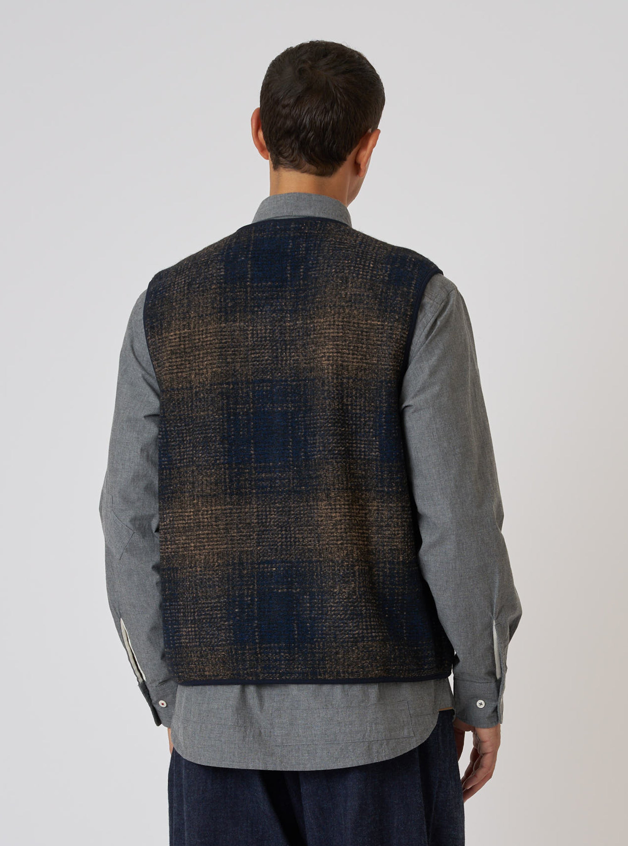 Back view of a model wearing a Navy Deca Check Zip Gilet. The gilet features a navy and brown check pattern. The model is wearing a grey shirt. Simple white studio background.