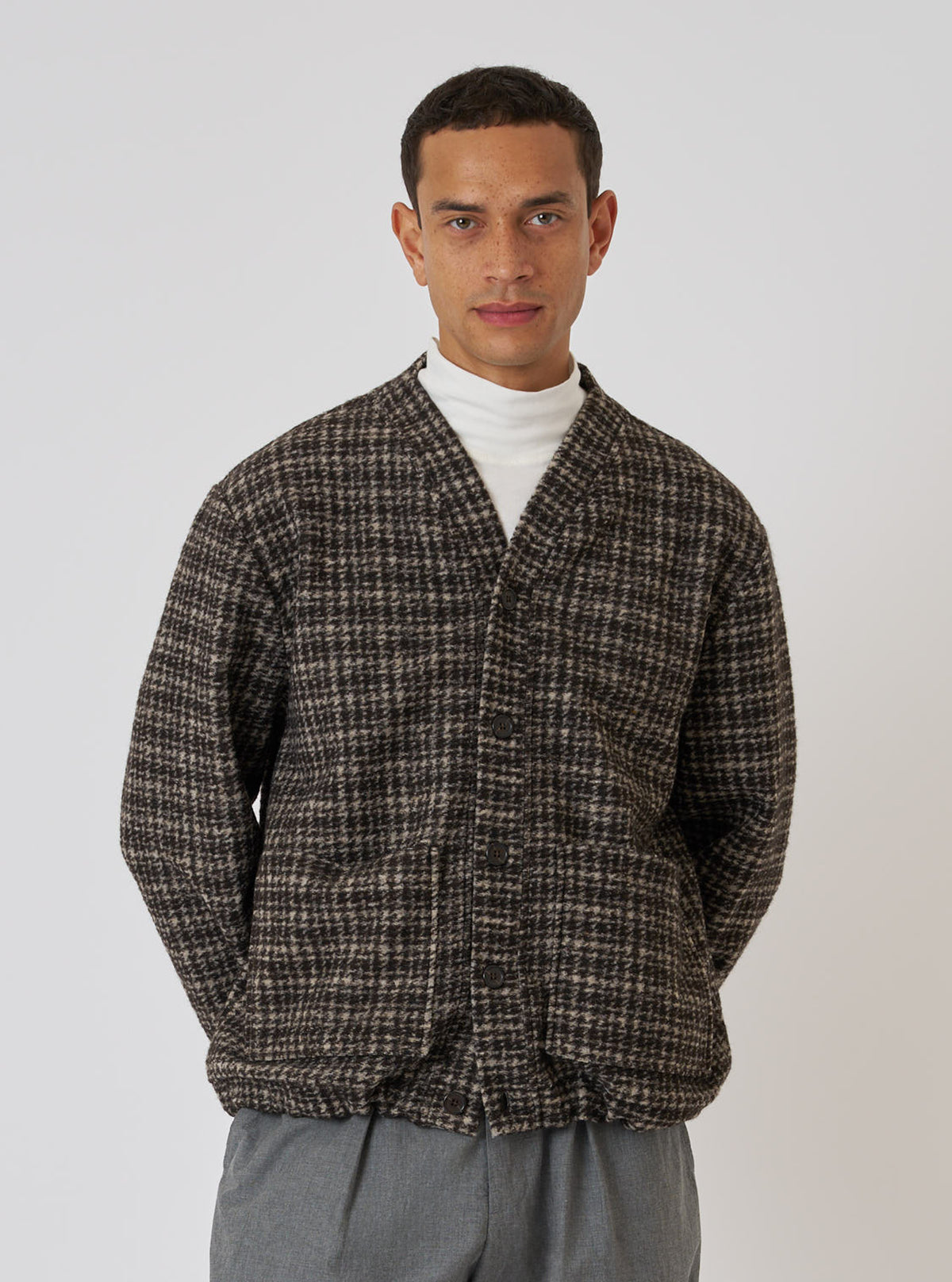 A model on a white background wears a Brown Jacquard Knit Advance Cardigan. The cardigan is brown with a jacquard knit pattern. He also wears a white turtleneck and grey pants.
