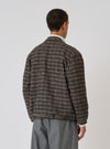 A man stands against a white backdrop, modeling the Brown Jacquard Knit Advance Cardigan. The cardigan features a brown and beige pattern. He wears gray pants.