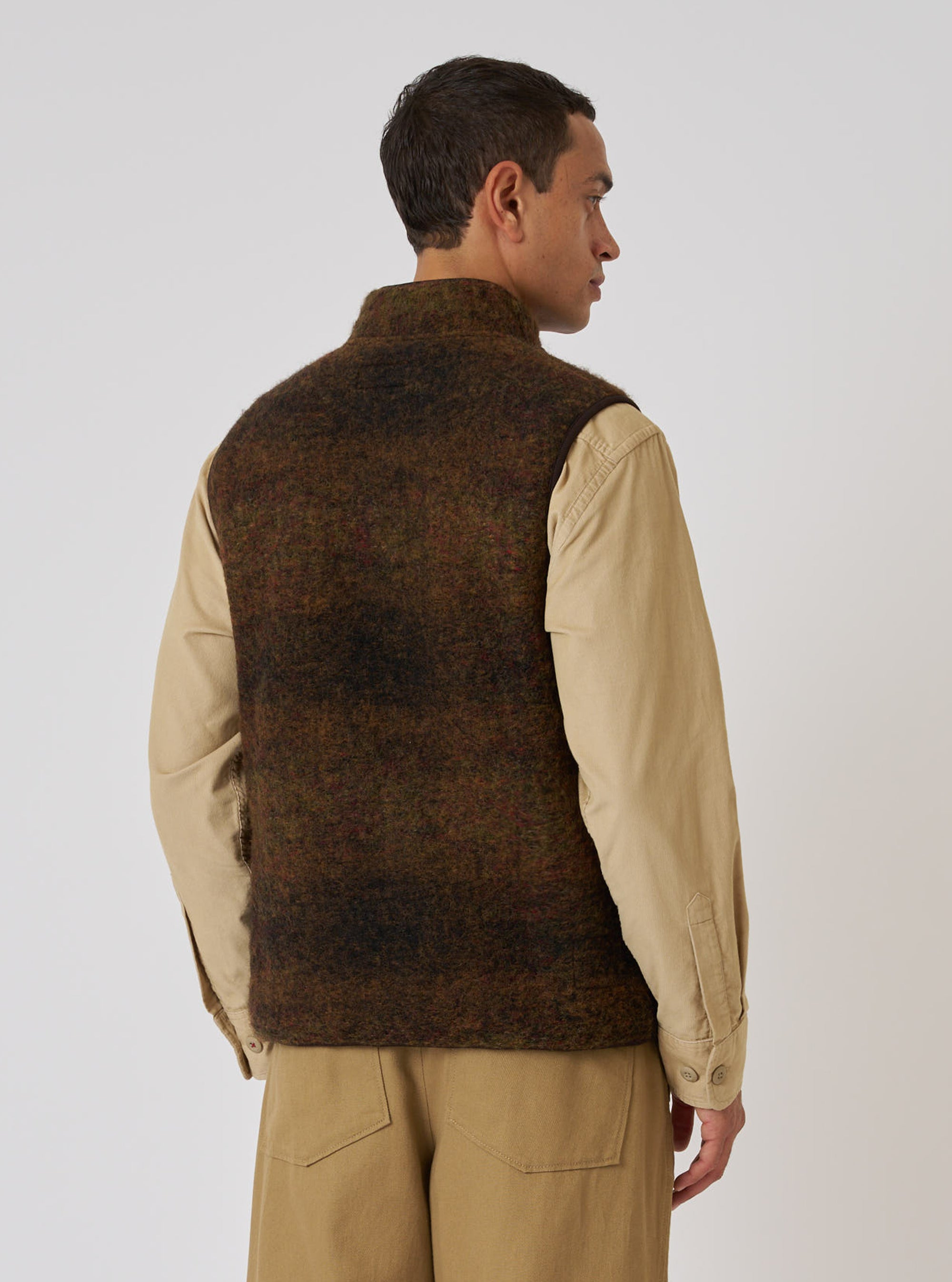 A man in profile wears the Brown Alps Fleece Climbing Gilet over a tan shirt and pants. The gilet is brown fleece. Shot against a plain white backdrop.