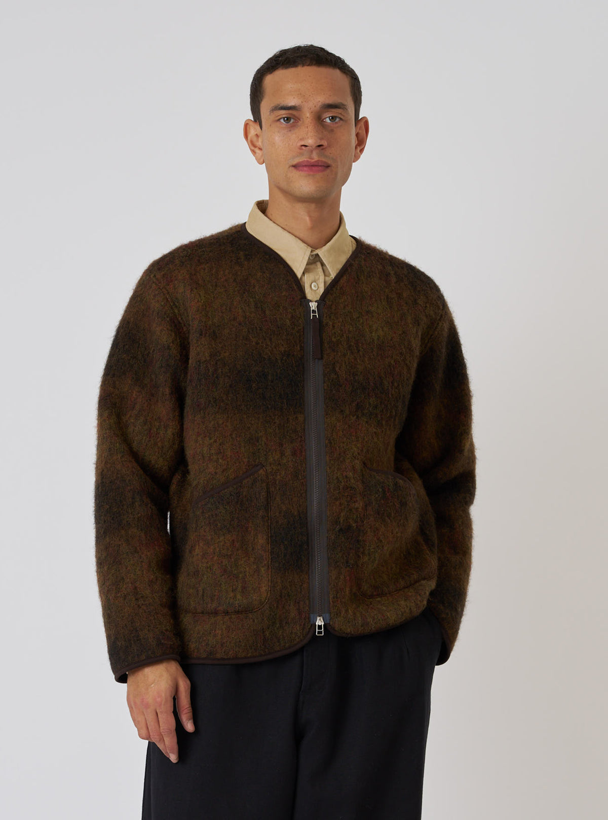 A man wears the Brown Alps Fleece Zip Liner Jacket in a studio shot against a white backdrop. The jacket is brown fleece with a zip front and trim.