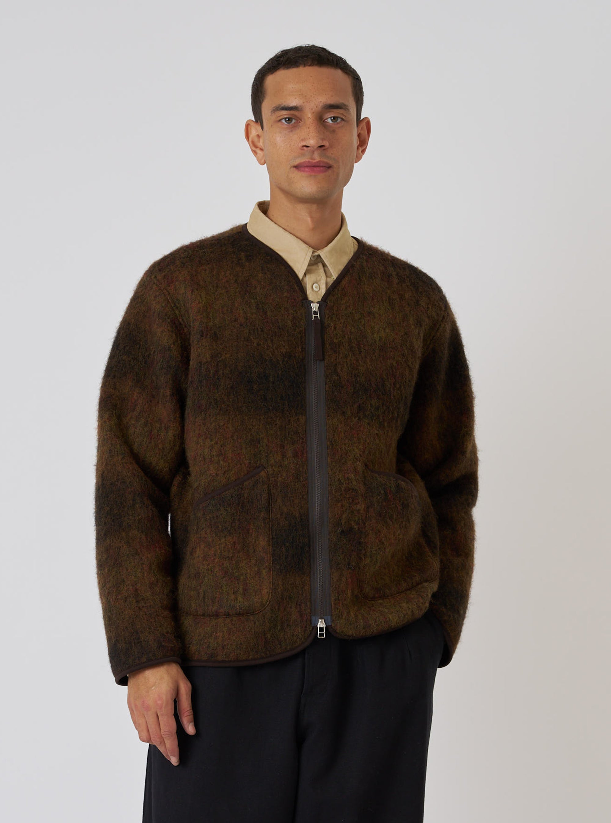 A man wears the Brown Alps Fleece Zip Liner Jacket in a studio shot against a white backdrop. The jacket is brown fleece with a zip front and trim.