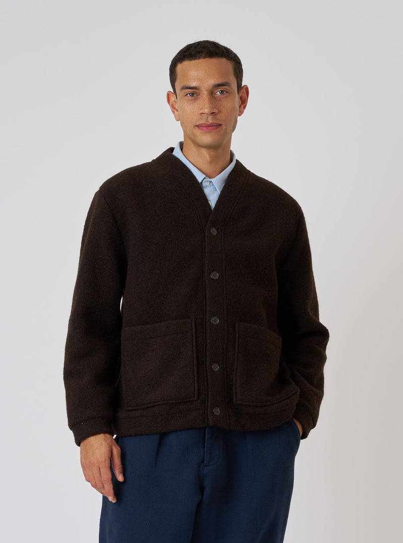 A model poses in front of a white background wearing a Brown Wool Fleece Advance Cardigan. The cardigan is paired with a light blue shirt and navy pants.