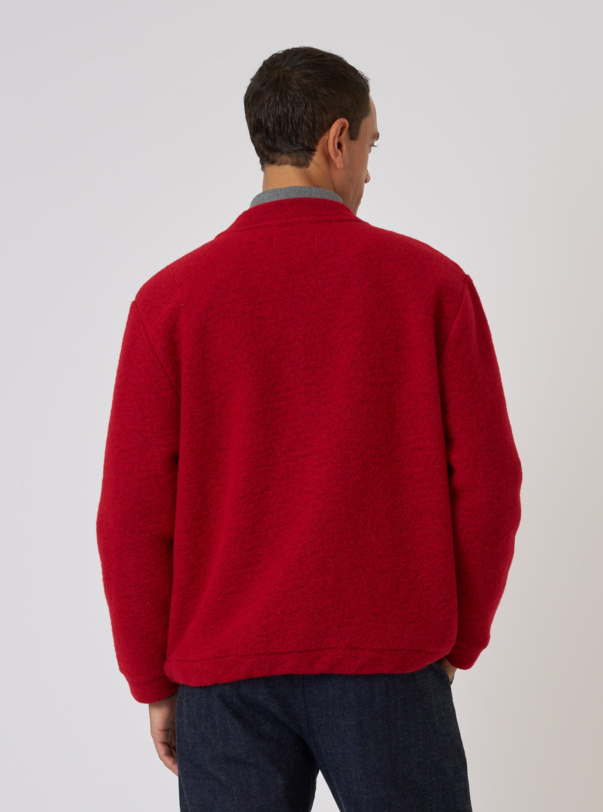 Back view of a man wearing a Red Wool Fleece Advance Cardigan. The fleece cardigan is paired with dark jeans against a plain white backdrop.