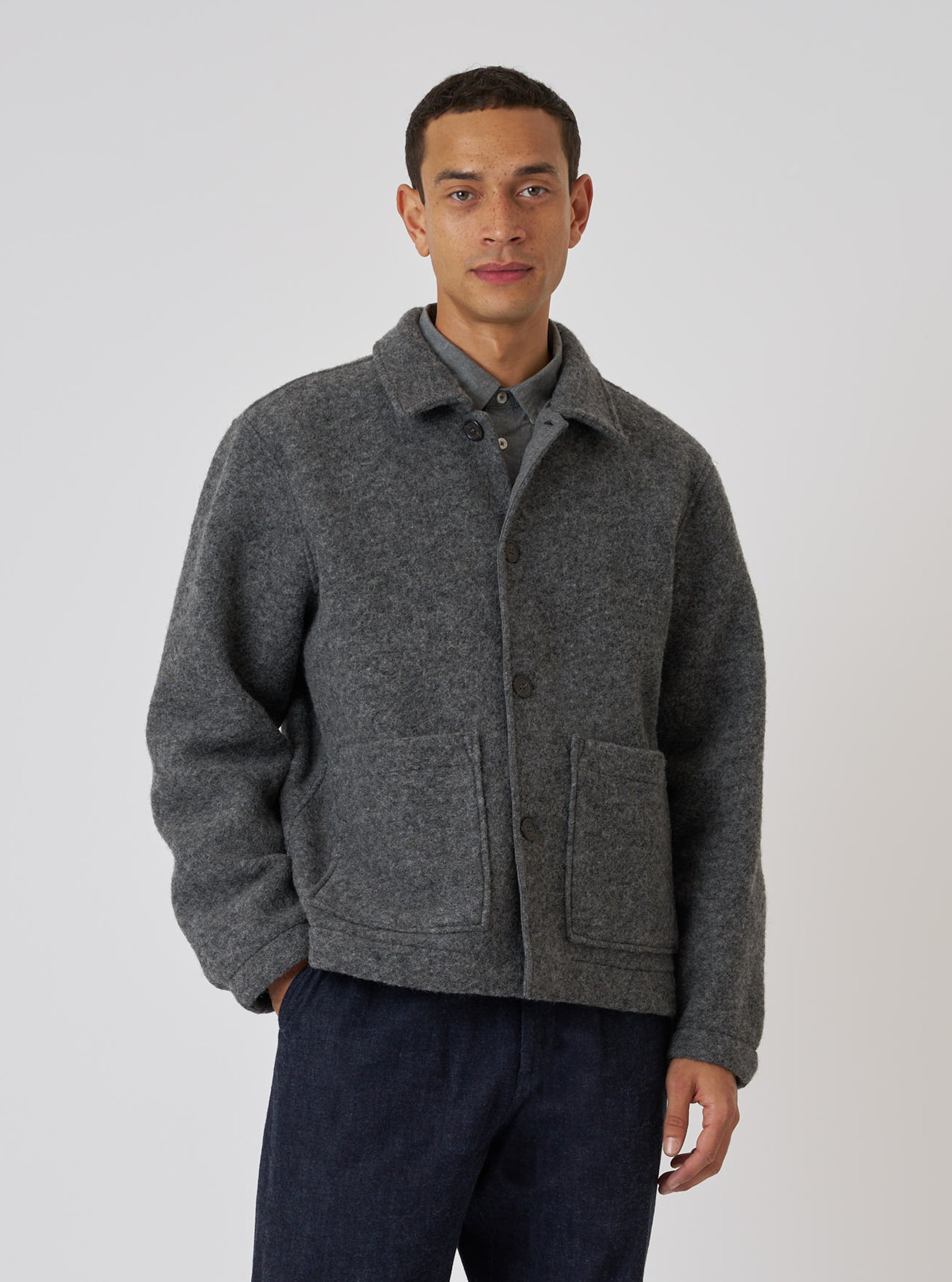 A man poses in front of a white background, wearing a Grey Marl Wool Fleece Rams Jacket. The jacket is wool with a button-up front and patch pockets.