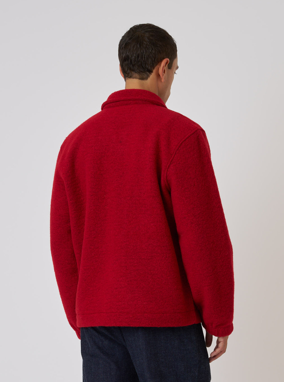Back view of a man wearing a Red Wool Fleece Rams Jacket. The jacket is bright red and made of a textured wool fleece. Shot against a plain white backdrop.