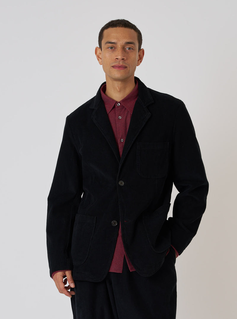 A model poses in a Black Cat Cord Two Button Jacket. The jacket is black corduroy, worn over a red shirt. The background is a plain white studio backdrop.