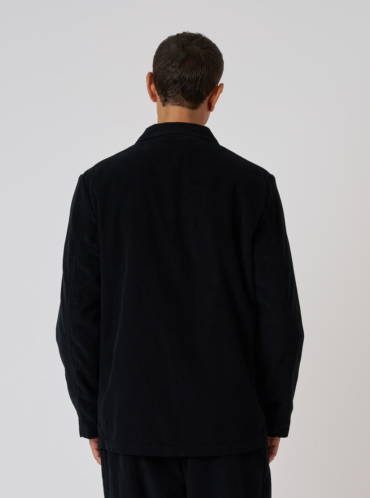 Back view of a model wearing a Black Cat Cord Two Button Jacket. The jacket is black corduroy, and the background is a plain white studio backdrop.