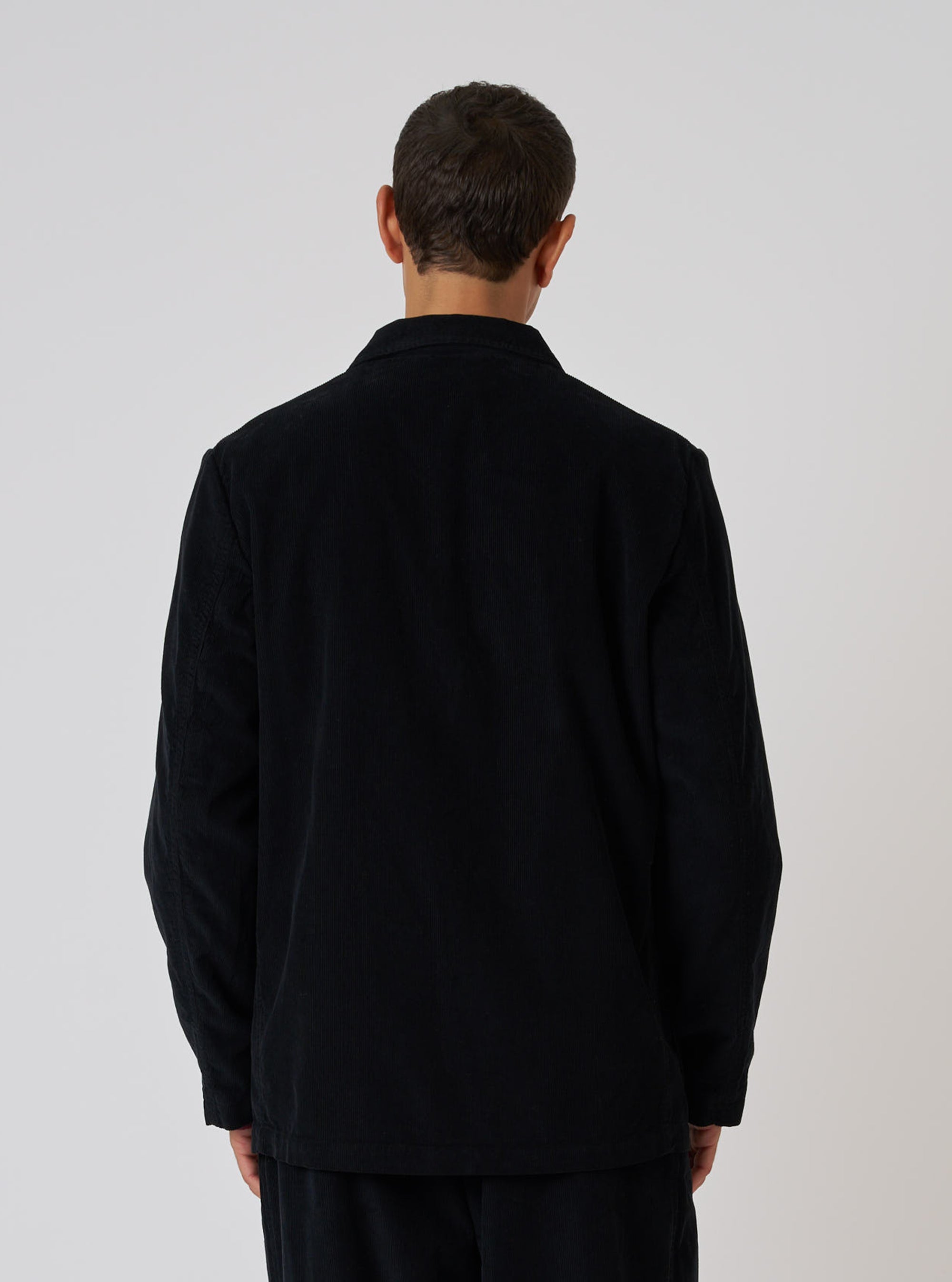Back view of a model wearing a Black Cat Cord Two Button Jacket. The jacket is black corduroy, and the background is a plain white studio backdrop.