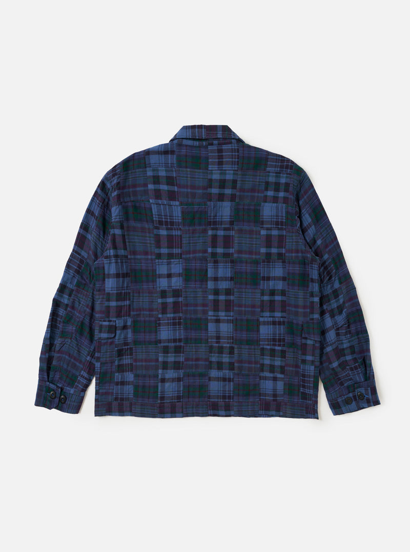 The Navy Madras Patchwork Duty Jacket is shown from the back, laid flat against a plain white background. The image highlights the patchwork construction of various blue and navy plaid cotton fabrics, the straight hem, and the loose, darted sleeves.