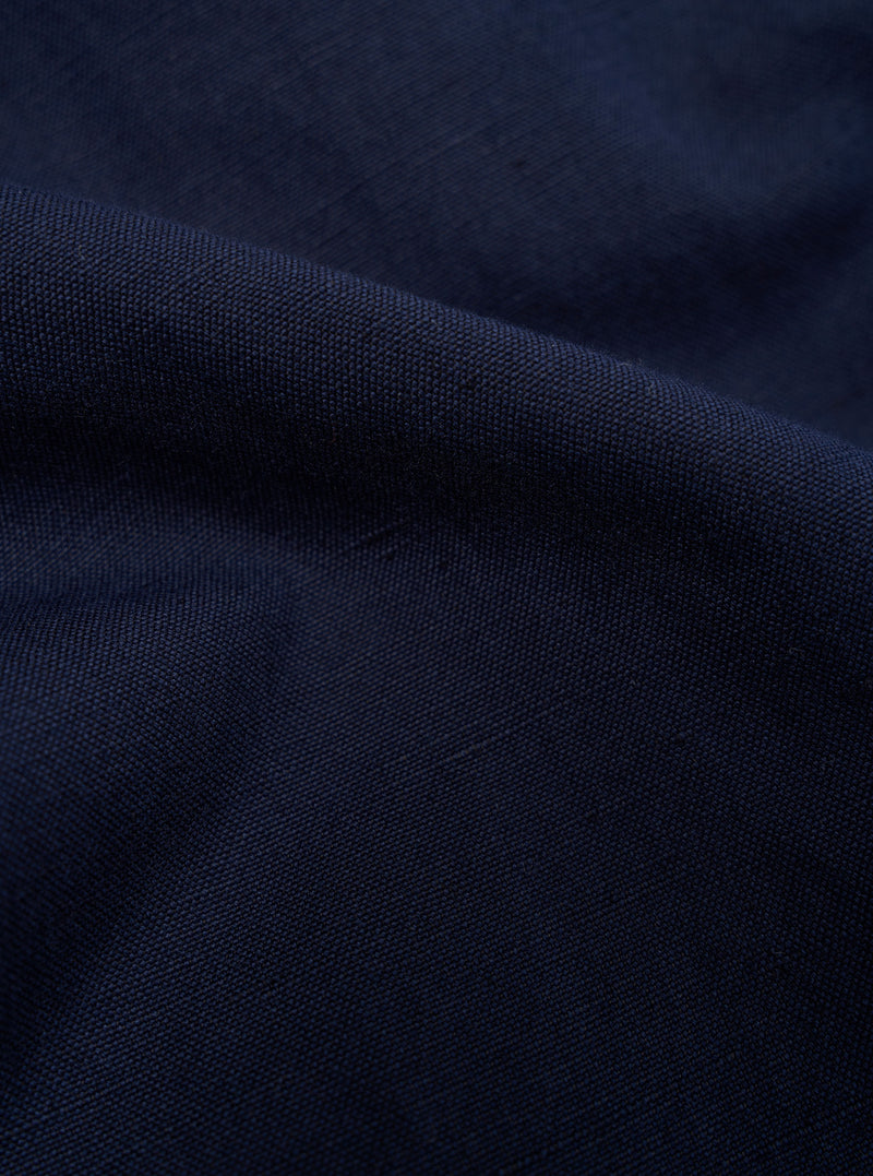 A close-up, square fabric swatch of the Navy Linen Slub Weave E130 Jacket highlights the detailed texture of the material. The fabric features a prominent slubbed yarn weave in a dark navy blue color, creating a slightly uneven and tactile surface. The swatch is shown as a flat, detailed material sample.