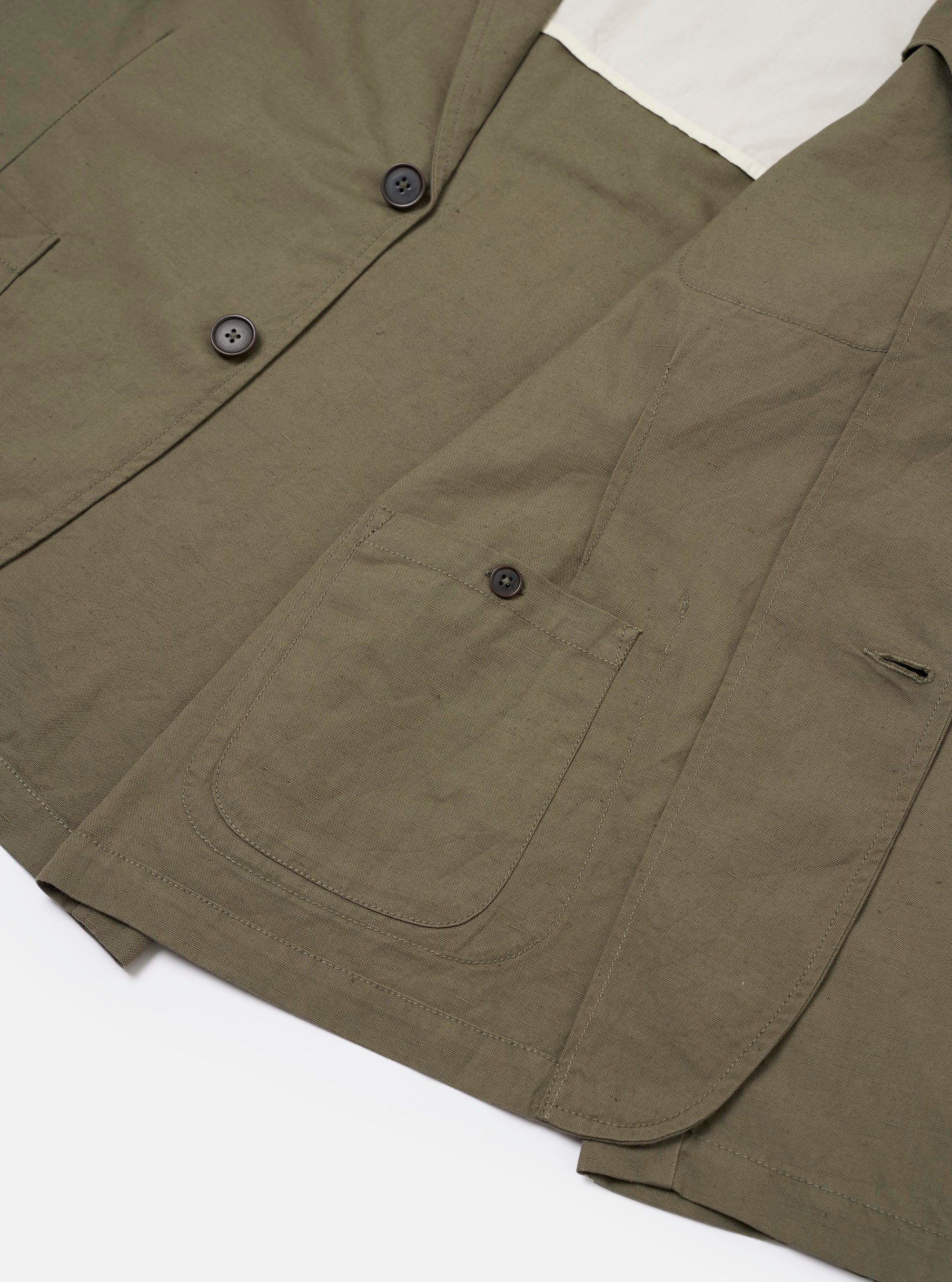 The Olive Linen Slub Weave Two Button Jacket is shown in a detail view as a flat lay against a plain white background. The image highlights the textured slub weave of the olive green linen-blend fabric and the construction of the straight side flap pockets and the two-button front closure.