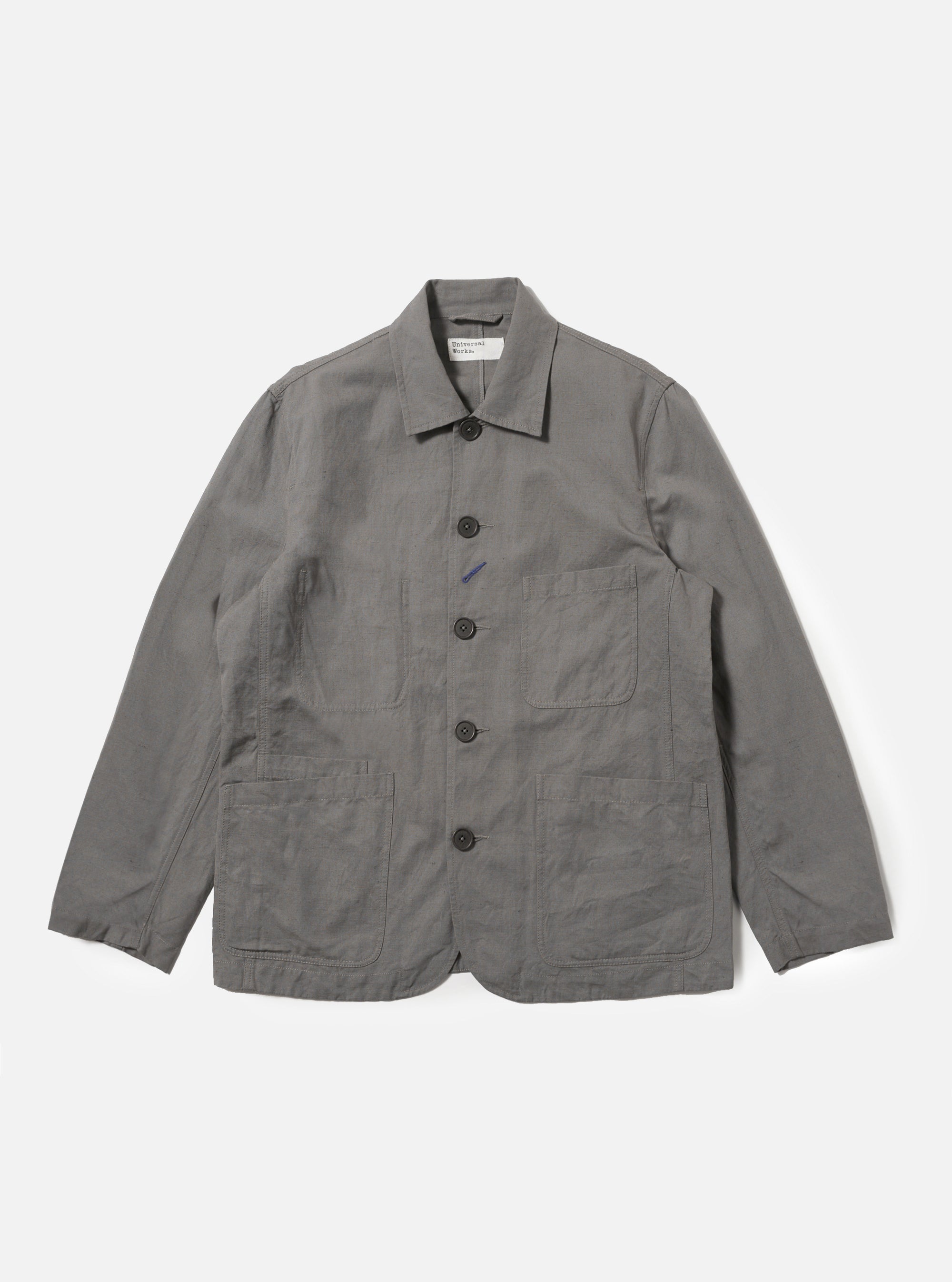 The Mid Grey Linen Slub Weave Bakers Jacket is shown as a flat lay against a plain white background. The jacket features a five-button front closure, a structured collar, and four asymmetrical patch pockets on the front, including one with a buttoned flap. The mid-grey fabric has a visible slubbed texture from the linen and cotton blend.
